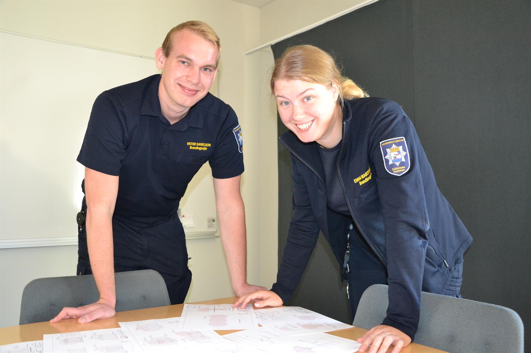 En man och en kvinna, båda klädda i räddningstjänstens uniform, står lutade över ett bord.